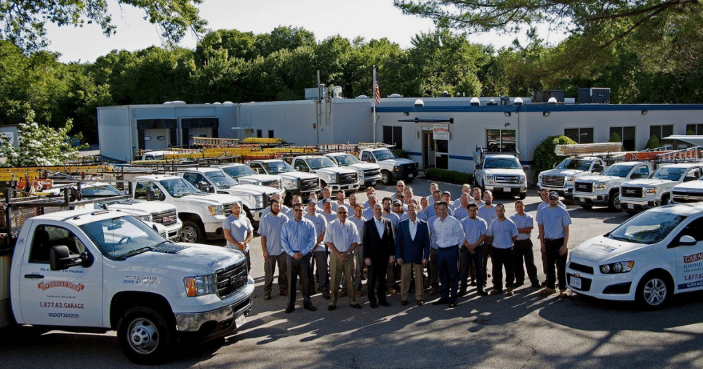 Employees from a garage door company pose with their fleet in a parking lot.