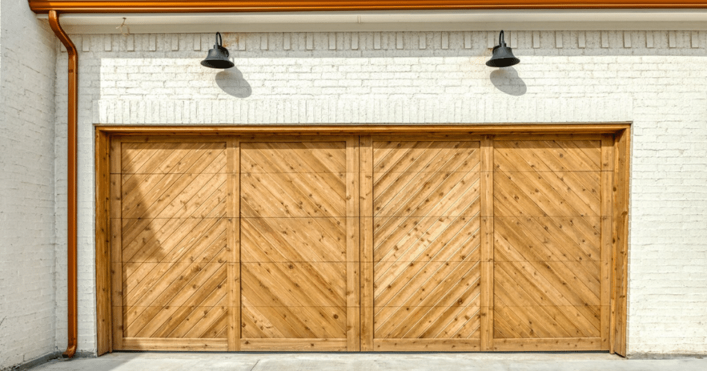 Wooden garage door on a white brick wall with two black lamps above.